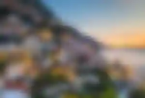 Italien Last Minute Angebote an der Amalfiküste Bunte Häuser an einem steilen Küstenhang der Amalfiküste in Italien bei Sonnenuntergang mit Blick auf das Mittelmeer.