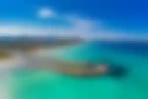 Traumbucht auf Mallorca mit türkisblauem Meer Panoramaaufnahme einer türkisblauen Bucht auf Mallorca mit geschwungener Landzunge, Sandstrand, Hotels im Hintergrund und Bergen am Horizont unter blauem Himmel.